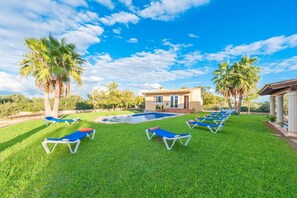 A pool area with lounge chairs, palm trees, and a building with a tiled roof.