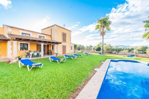 Zona de piscina con sillones de descanso y un edificio con tejado de azulejos.