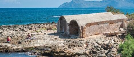 A stone structure with arched openings near a rocky shoreline and the sea.