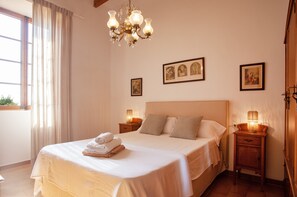A neatly made bed with a folded towel, a bedside table with a lamp, and a chandelier. - CAN CIREROL - Villa with private pool in Porto Colom- Felanitx. Free WiFi. (Portocolom)