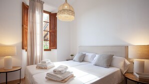 Ein ordentlich bezogenes Bett mit gefalteten Handtüchern, einer Nachttischlampe und einem Fenster mit Vorhängen.