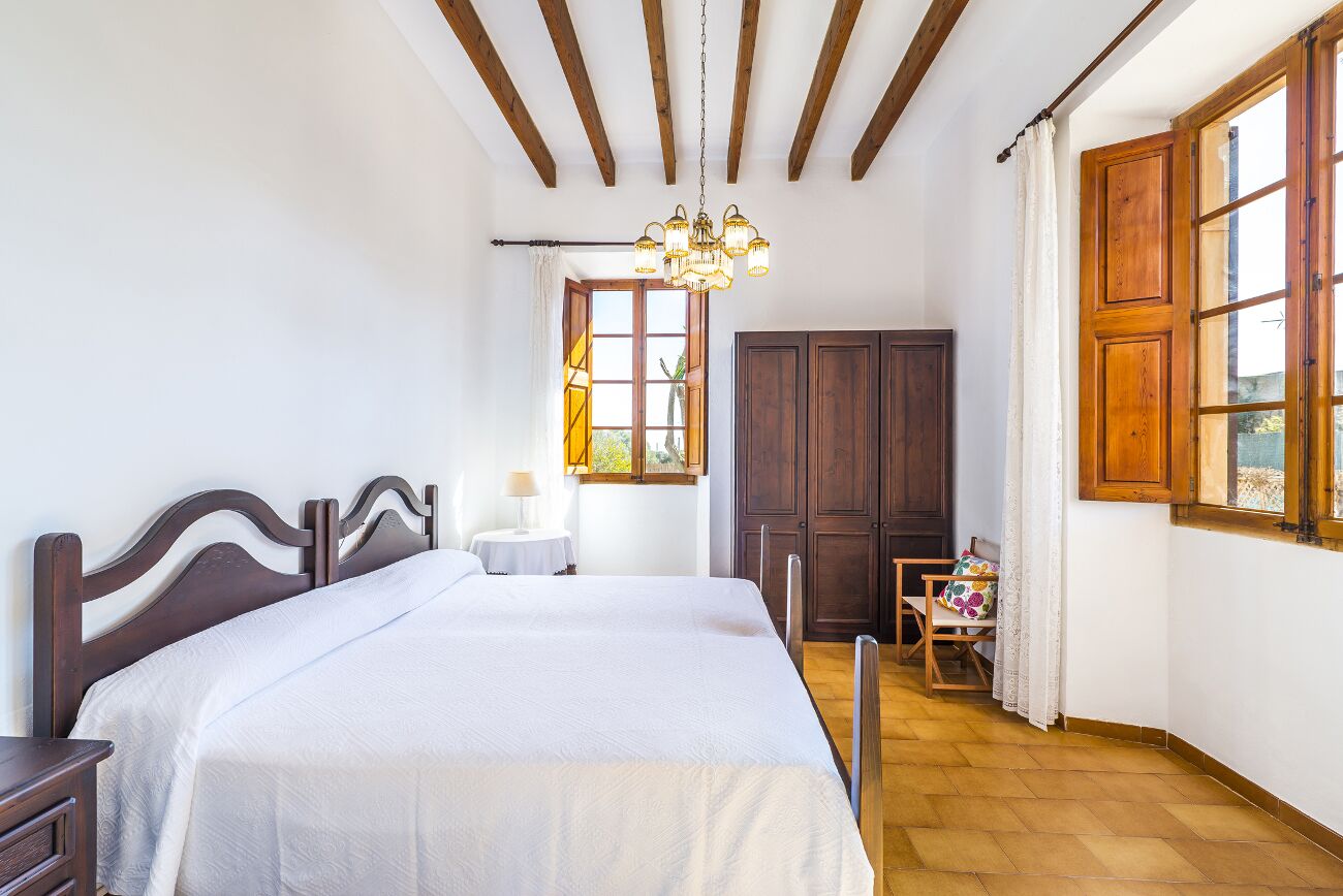 A bedroom with a wooden bed, a chandelier, a wardrobe, and a window with curtains.