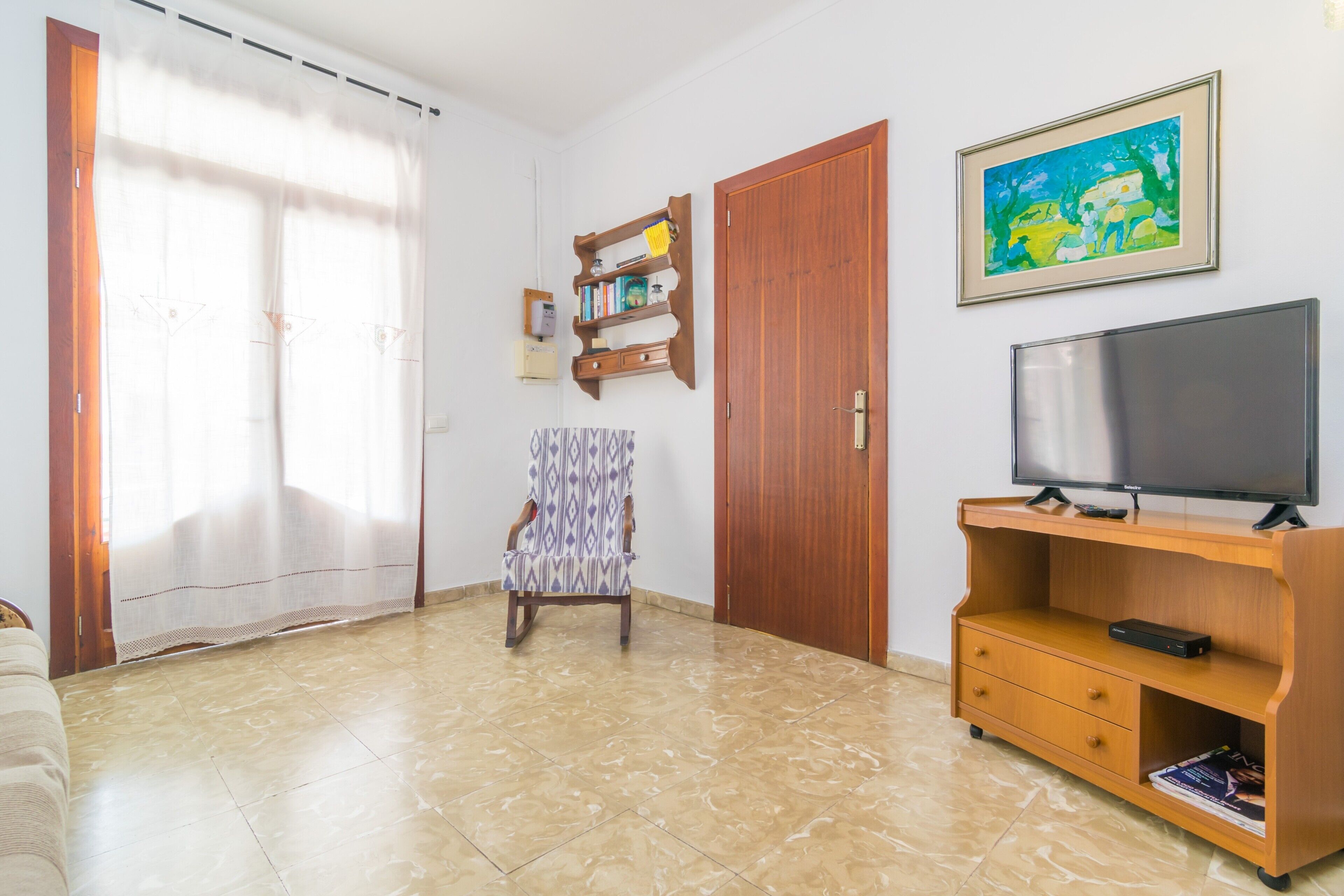Un soggiorno con un mobile porta televisione in legno, una poltrona con motivo decorativo, una libreria e un quadro appeso al muro.