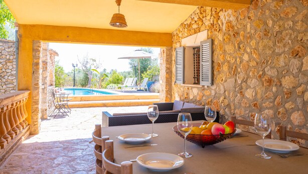 Uma área de refeições com parede de pedra, vista para a piscina e assentos ao ar livre.