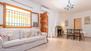 Sala de estar com sofá branco, mesa de jantar de madeira e cadeiras.