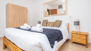 Quarto bem arrumado com uma cama grande, um guarda-roupa de madeira, uma mesa de cabeceira com abajur e um espelho na parede.