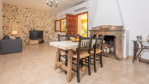 Uma área de refeições com parede de pedra, mesa de madeira e cadeiras. Há uma televisão e um sofá na sala de estar.