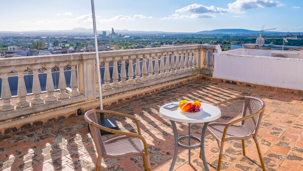 A balcony with a table and chairs, a view of a cityscape, and a clear sky.