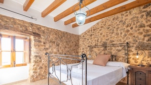 A bedroom with a stone wall, a metal bed frame, a wooden ceiling, and a window.