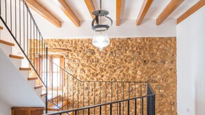 A staircase with a stone wall background, wooden beams, and a hanging light fixture.