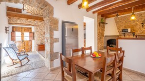 A rustic kitchen with a stone wall, wooden beams, a stainless steel refrigerator, and a dining table with chairs.