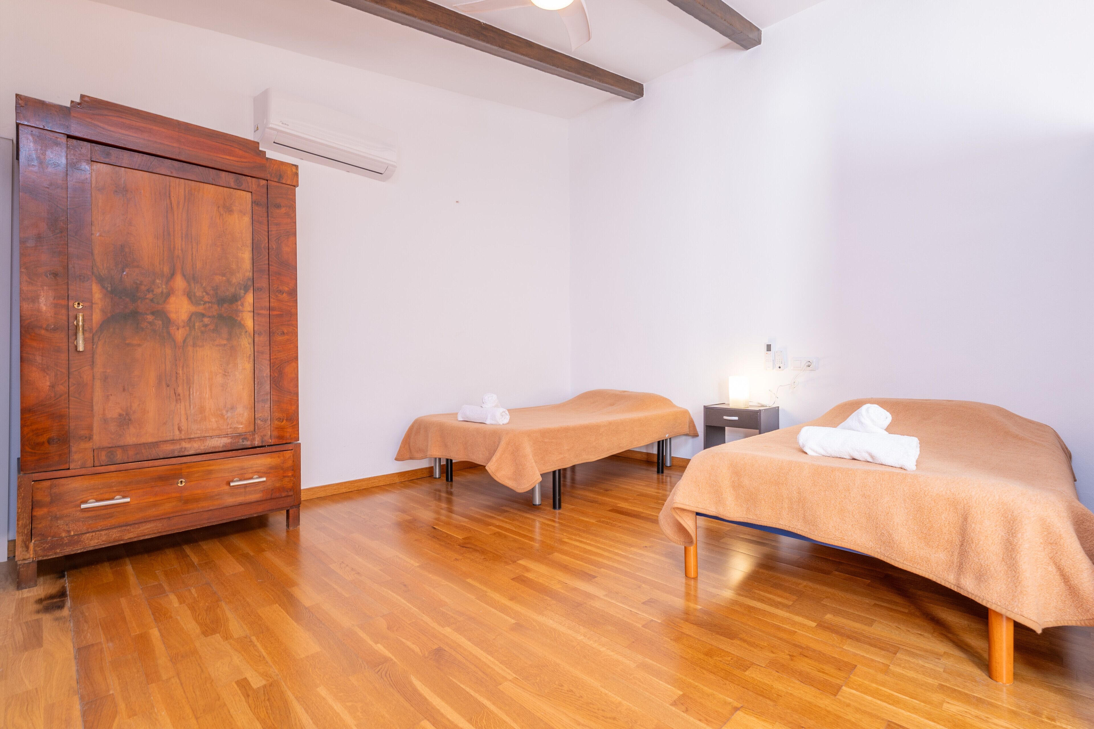 Una habitación con dos camas, un armario de madera y una mesita de noche con lámpara.