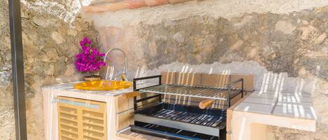 An outdoor grill setup with a stone wall backdrop, a metal grill, and a yellow tray.