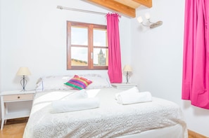 Une chambre à coucher avec un lit, deux tables de chevet, une fenêtre donnant sur un paysage agréable et un rideau.