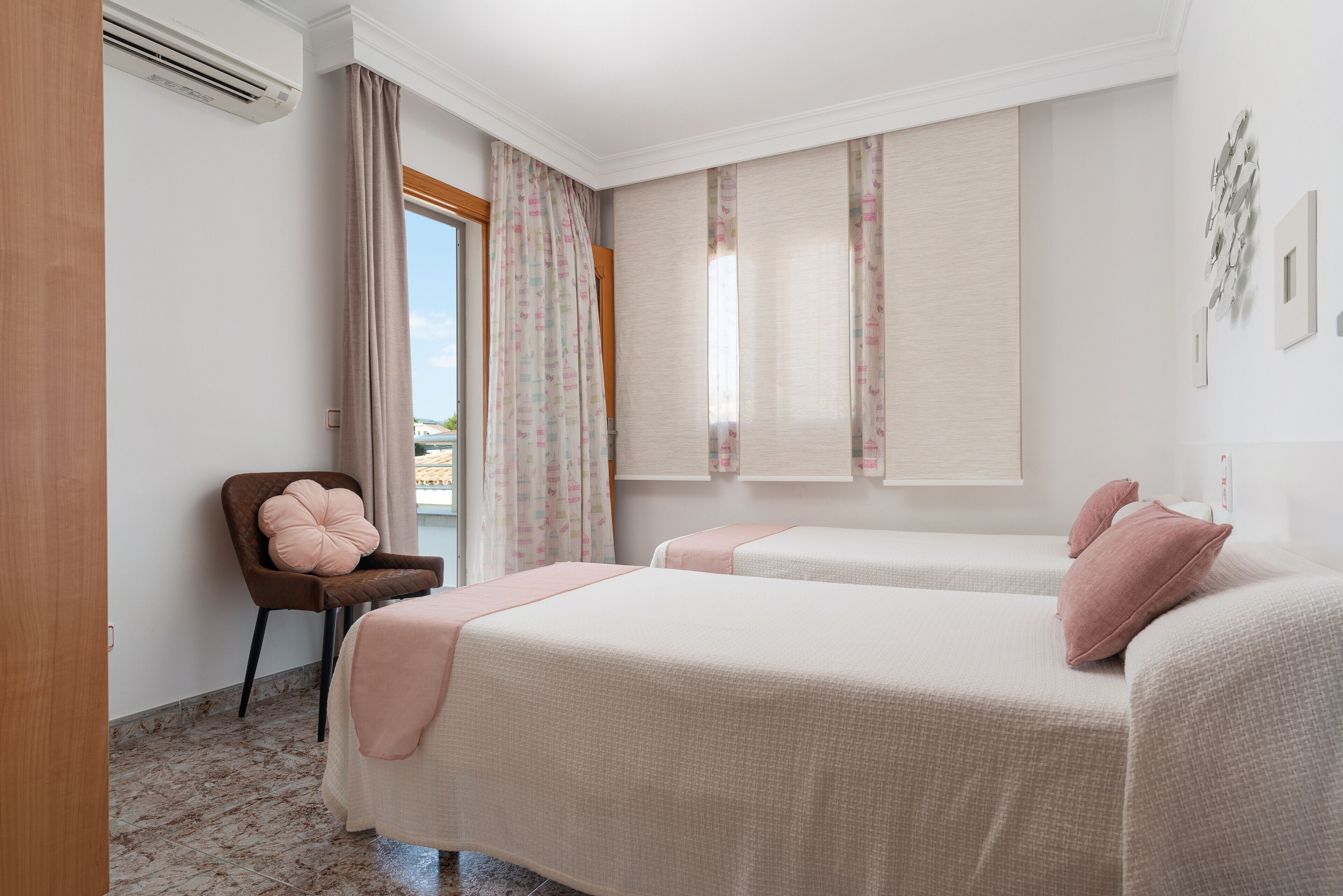 A hotel room with two beds, a chair, and a window with curtains.
