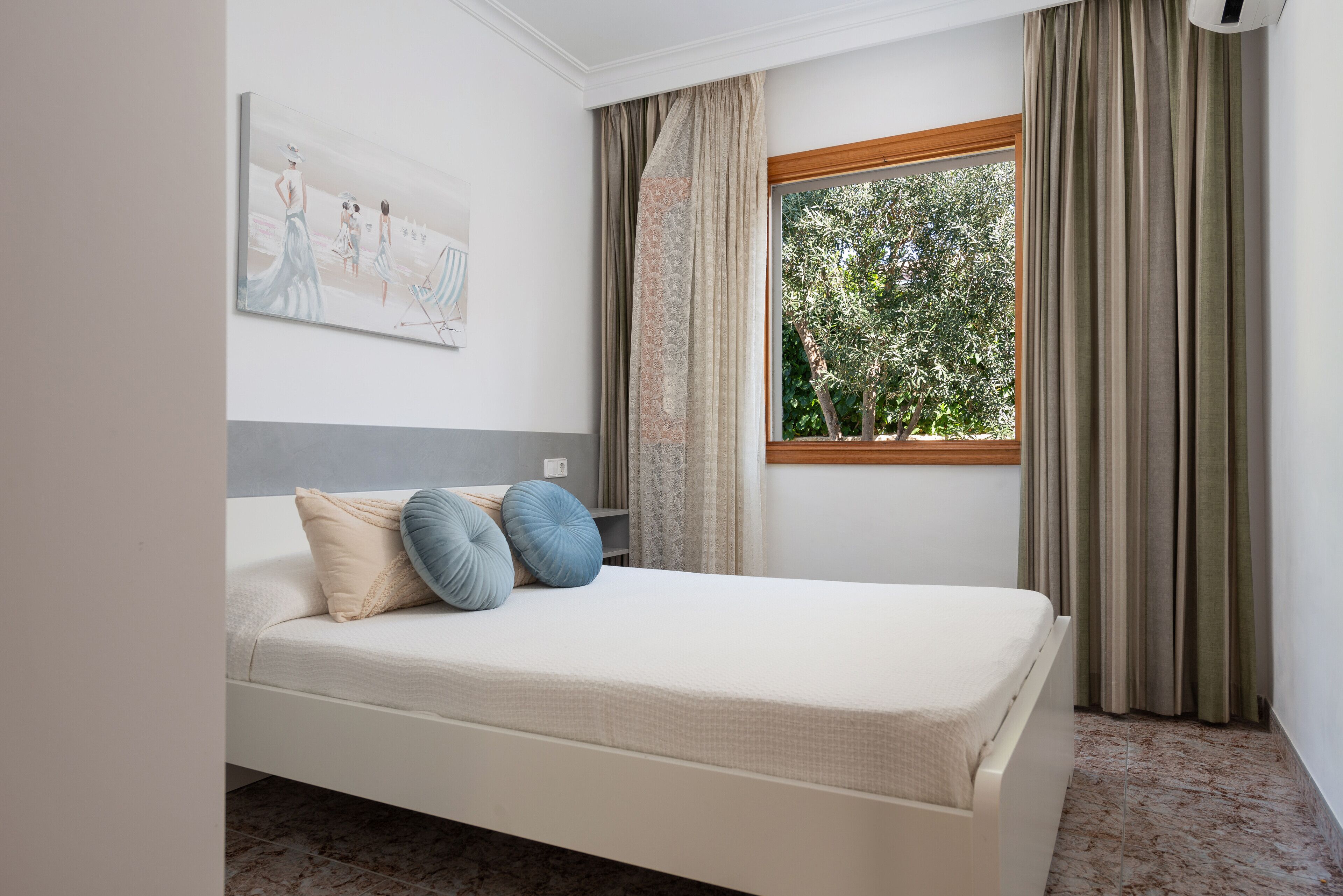 A bedroom with a bed, a window with curtains, a painting on the wall, and a ceiling fan.