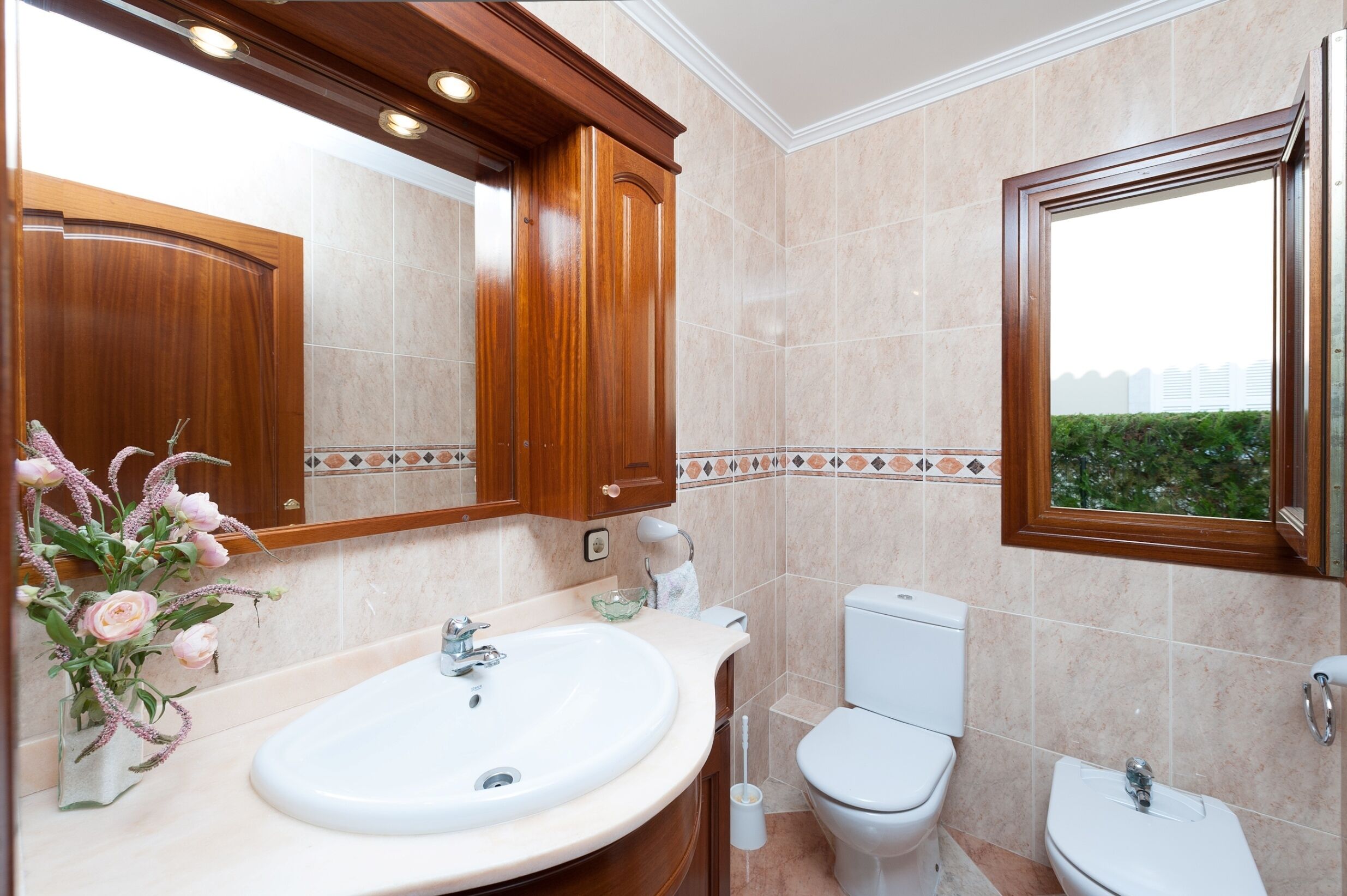 Un baño con un espejo grande, armarios de madera, un lavamanos blanco y un inodoro.