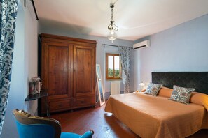 A bedroom with a large wooden wardrobe, a bed with patterned pillows, and a window with curtains.