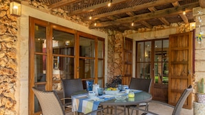 An outdoor dining area with stone walls, wooden doors, wicker chairs, and a table set with a tablecloth and various dishes. - SES TENDES - Villa with private pool and beautiful garden. Free WIFI (Algaida)