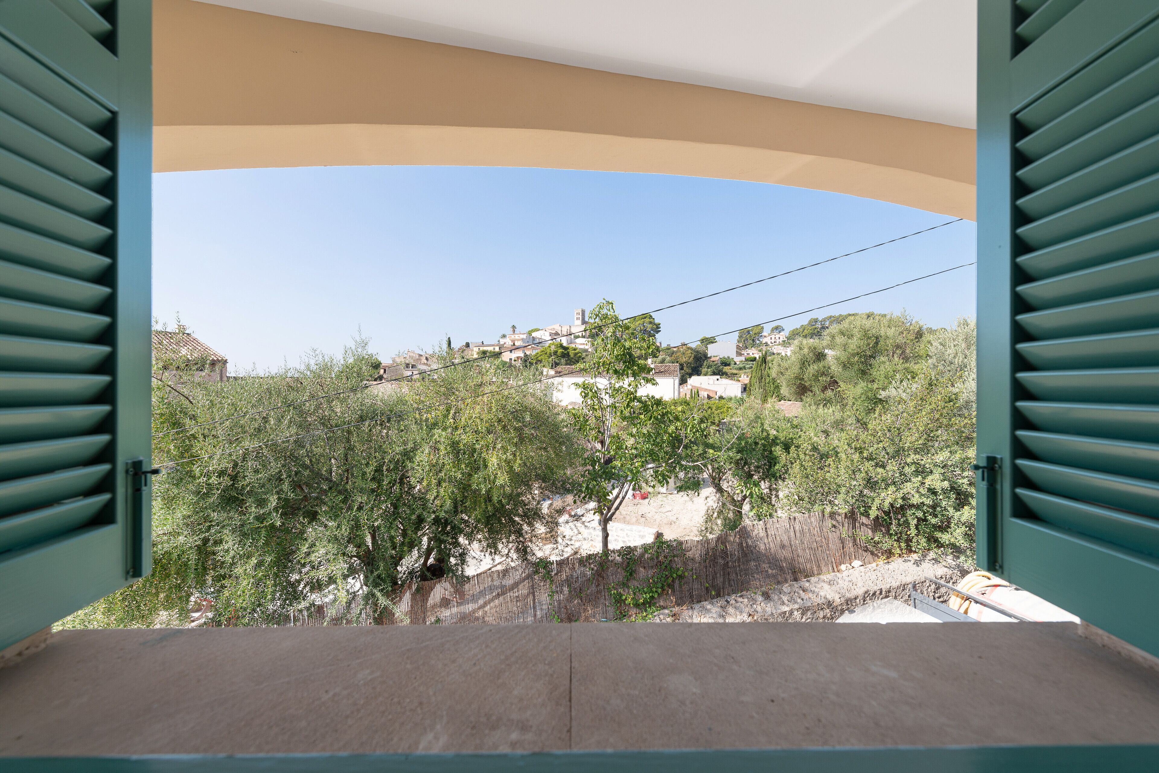A balcony with a view of a hillside town, a clear sky, and a fence in the foreground.