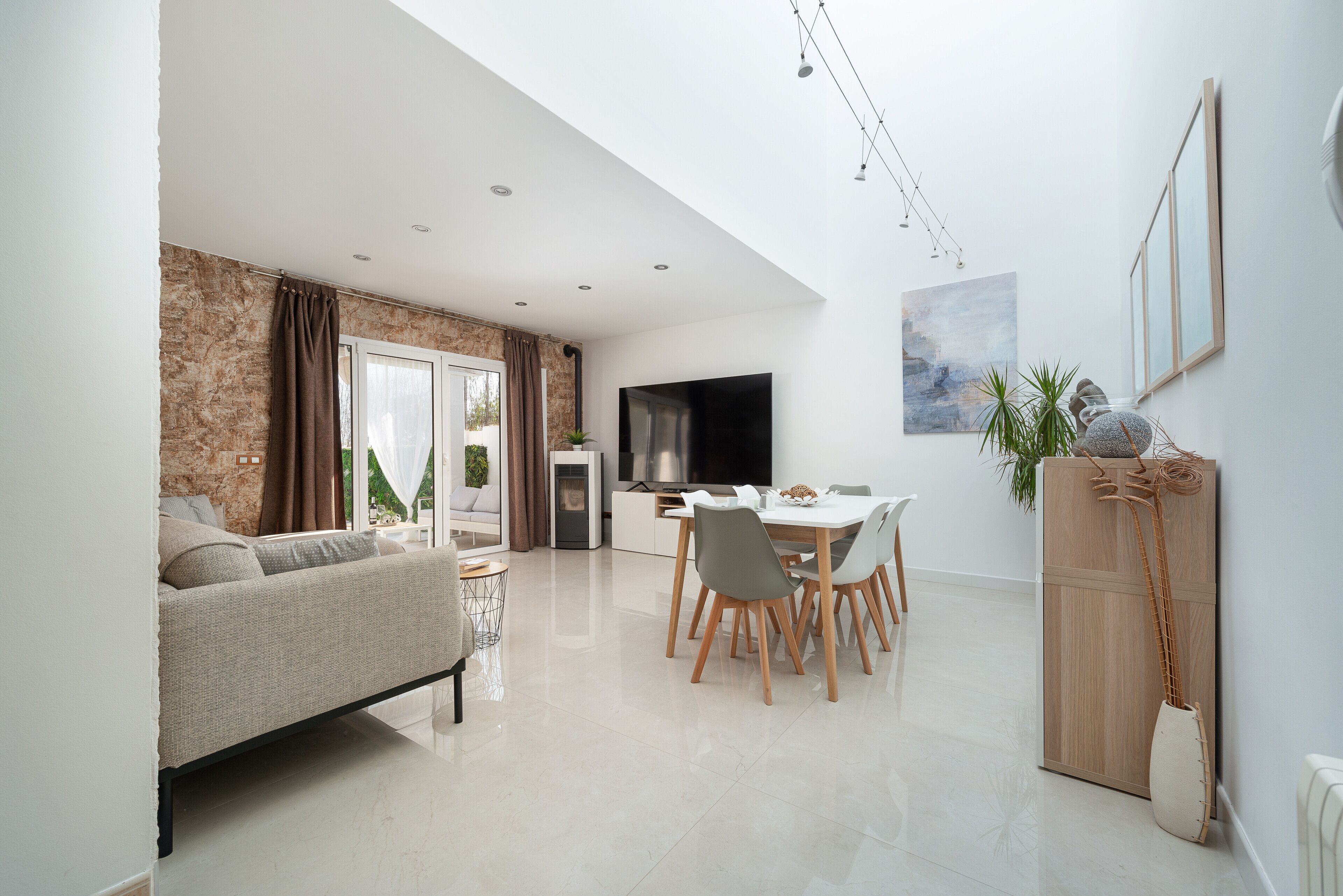 Una sala de estar moderna con un sofá, una mesa de comedor y sillas. Hay un televisor montado en la pared, una planta y una chimenea.