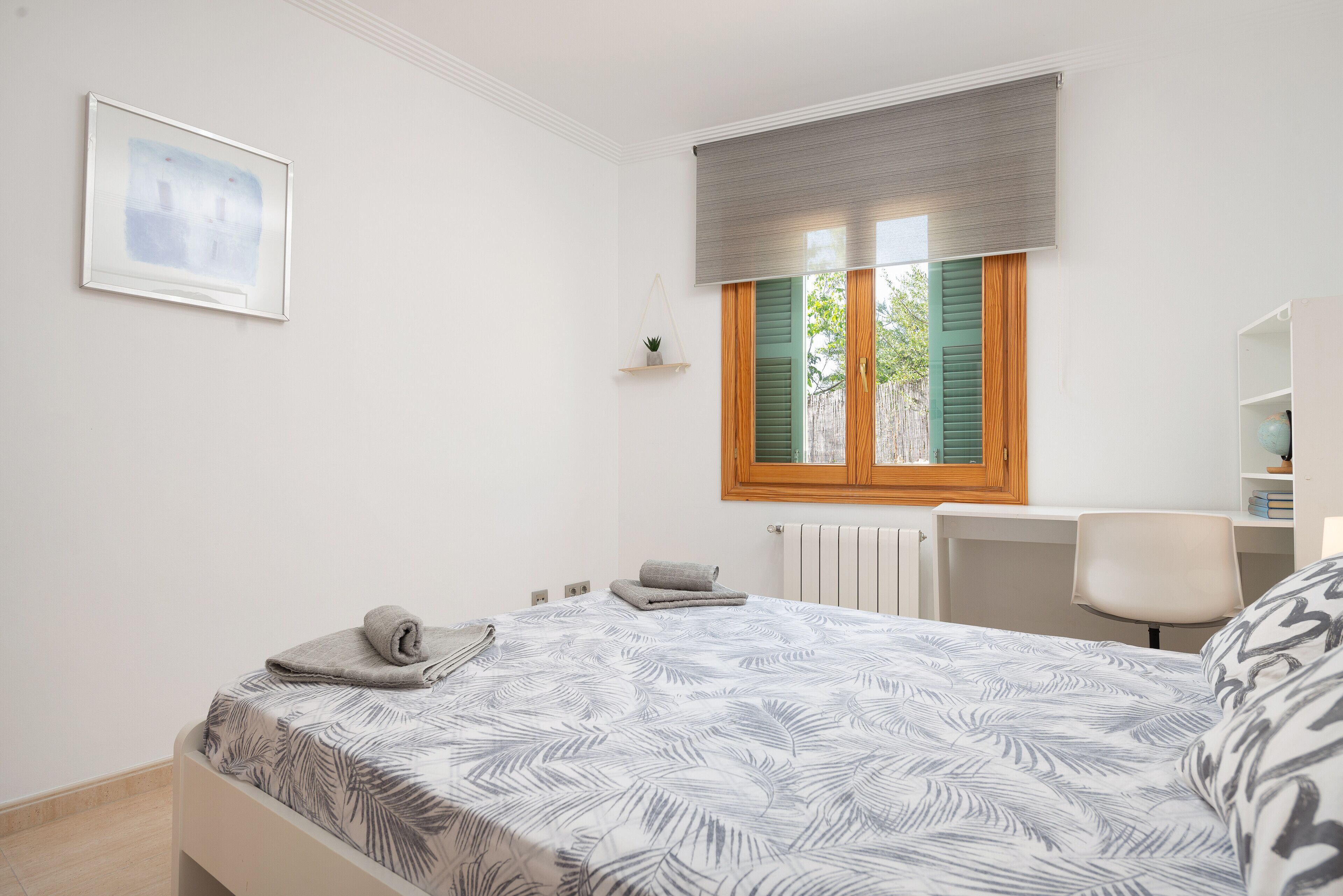 A bedroom with a bed, a desk, a chair, a radiator, and a window with shutters.