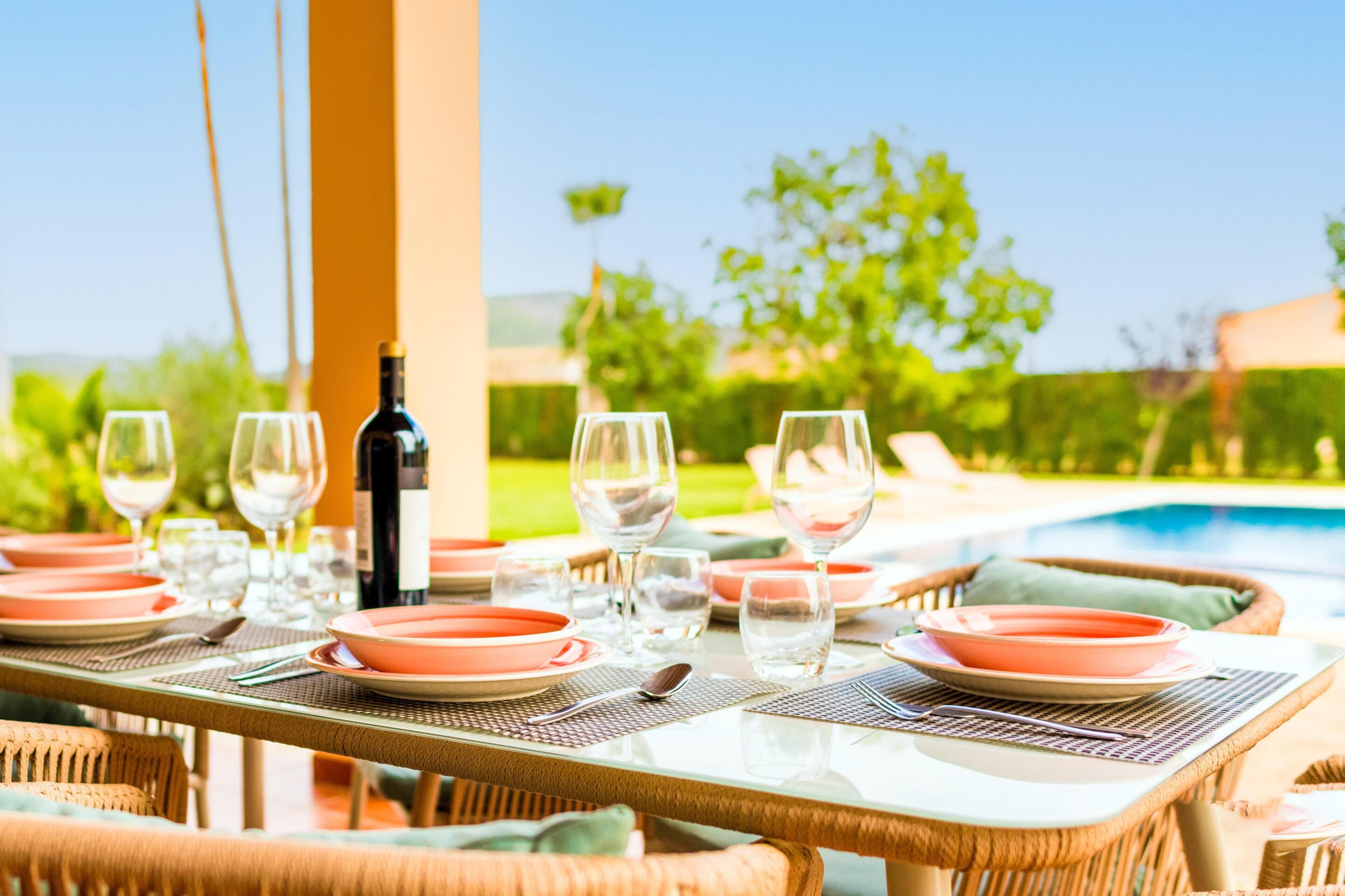 A dining table set outdoors with a pool in the background.