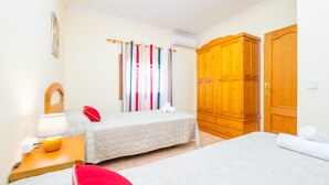 Ein Hotelzimmer mit zwei Betten, einem Holzschrank, einer wandmontierten Klimaanlage und einem Nachttisch mit Lampe.
