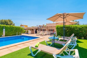 A swimming pool with lounge chairs and a table, surrounded by a hedge and a building with a tiled roof. - CAN TOMEU - Beautiful villa with private garden and pool in a quiet area. Free WiFi (Inca)