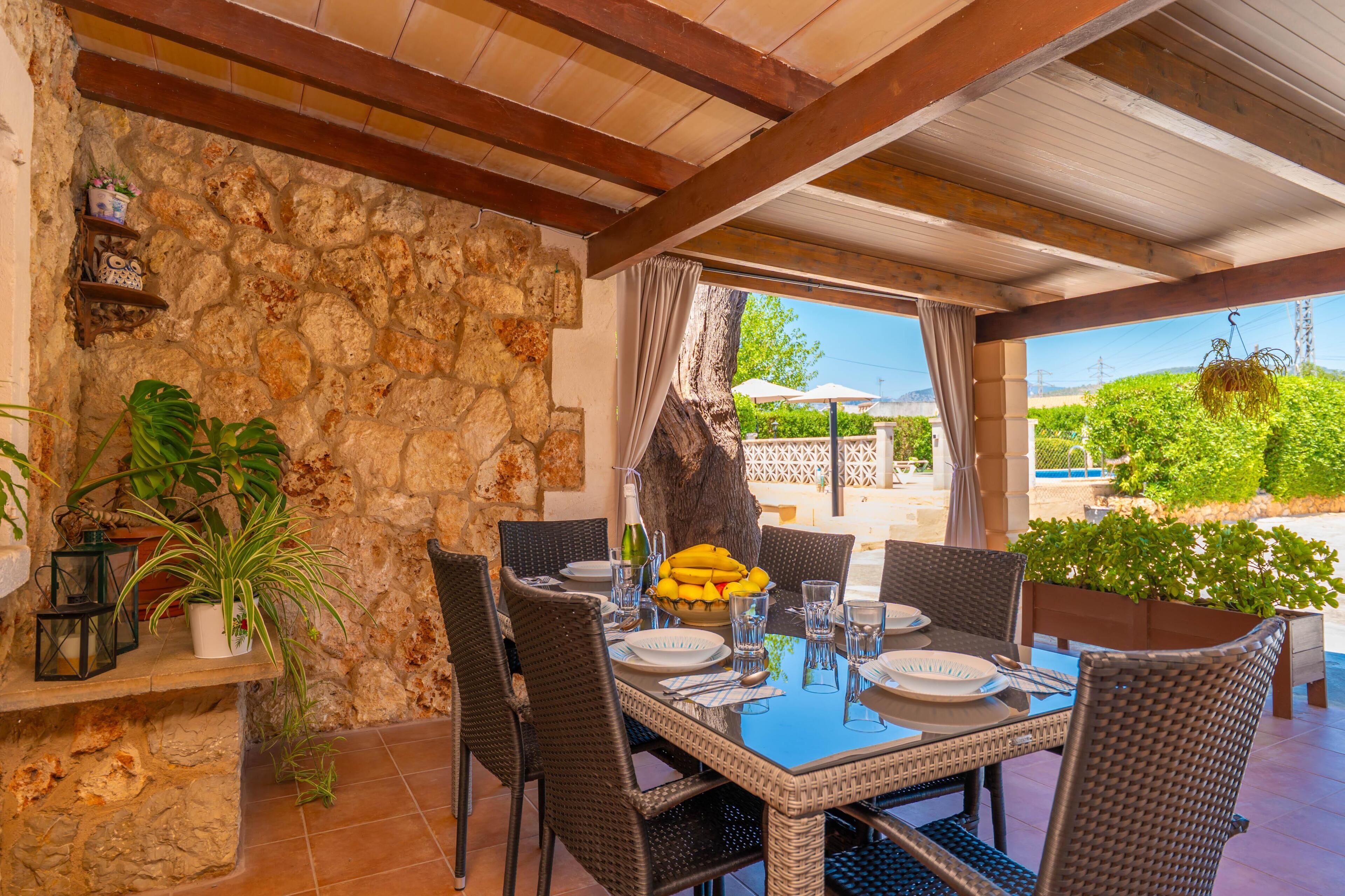 An outdoor dining area with stone walls, wicker furniture, and a view of greenery and a pool.