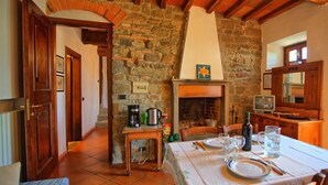 A rustic kitchen with a stone wall, a fireplace, a coffee maker, and a dining table set for two. - Apartment with pool, WIFI, TV, patio, pets allowed, panoramic view, close to Greve In Chianti (San Polo In Chianti)