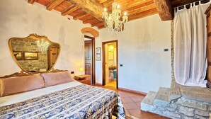 A bedroom with a large bed, a mirror, and a chandelier. There is a door leading to a bathroom. - Apartment with pool, WIFI, TV, patio, pets allowed, panoramic view, close to Greve In Chianti (San Polo In Chianti)