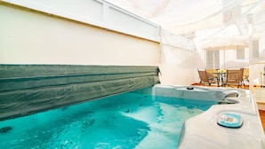 Ein Whirlpool mit Bedienfeld, eine Holzbank und ein Tisch mit Stühlen in einem sonnendurchfluteten Raum.