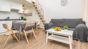 Ein modernes Wohnzimmer mit einem grauen Sofa, einem Esstisch mit Stühlen, einer Treppe und einer Wanduhr.