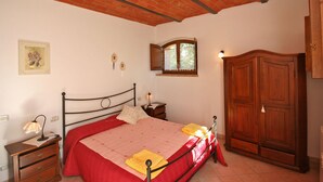 A bedroom with a bed, a wooden wardrobe, a nightstand, a lamp, and a window with a view of greenery. - Cosy apartment for 4 guests with WIFI, pool, TV and panoramic view, close to Montepulciano (Monticchiello)