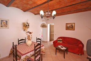 Un salon avec un canapé rouge, une table à manger avec des chaises, un lustre et un téléviseur.