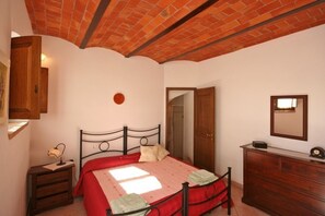 Une chambre avec un plafond en briques, un lit recouvert d’une courtepointe rouge, une commode en bois et un miroir au mur.