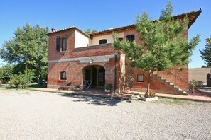 Un bâtiment à deux étages avec une façade en briques, une entrée centrale surmontée d’une arche et un petit porche aménagé avec des sièges.