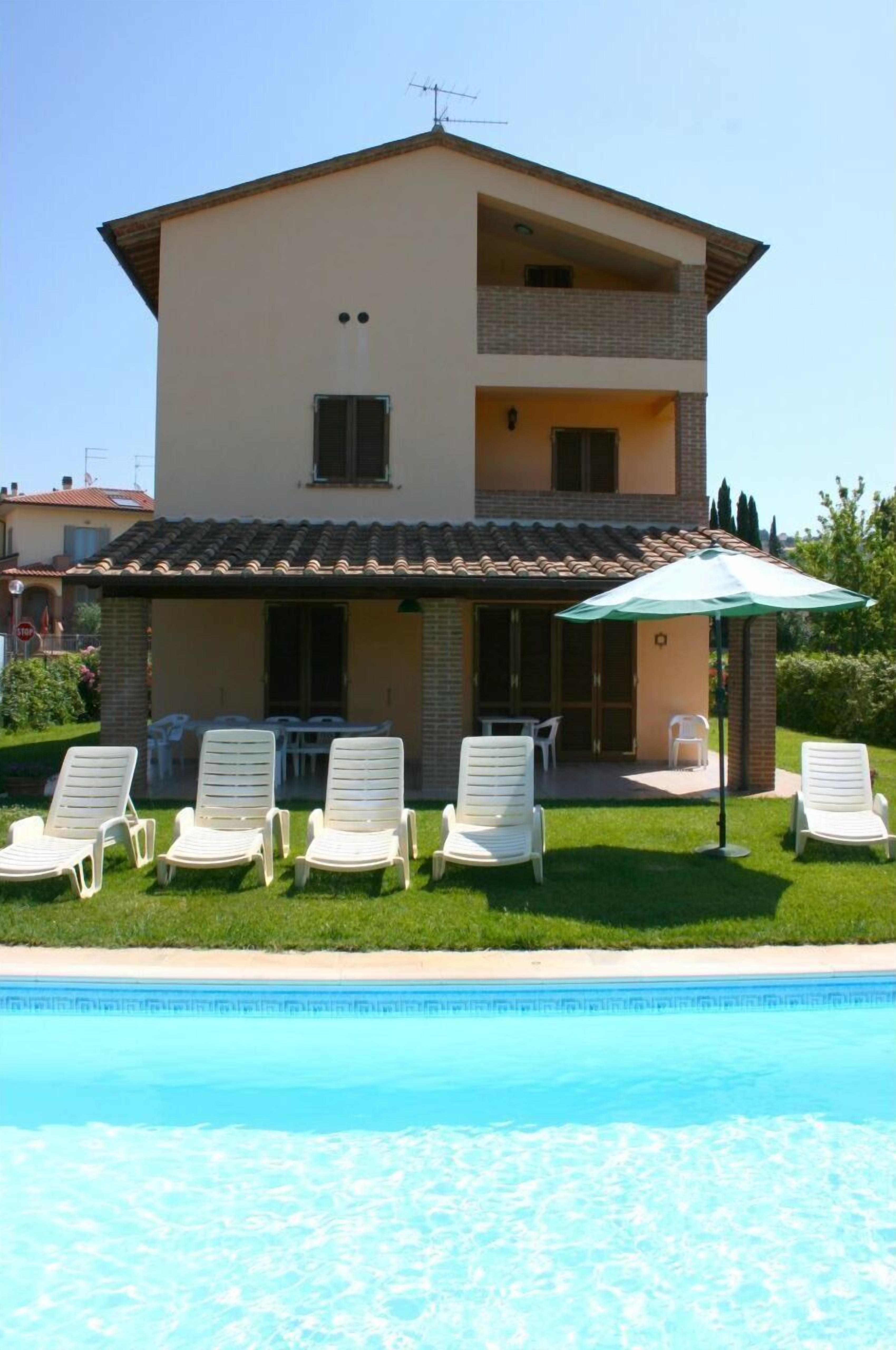 Ein zweistöckiges Haus mit Swimmingpool, Sitzgelegenheiten im Freien und einer überdachten Terrasse.