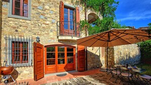 Un bâtiment en pierre avec une porte en bois, un balcon et un patio aménagé avec des sièges d’extérieur.