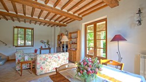 Une pièce chaleureuse avec un plafond en bois, un canapé à motifs floraux, une table à manger agrémentée d’un vase de fleurs et un buffet en bois doté d’étagères.