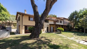 A two-story house with a large tree in the front yard, a patio area, and a small garden. - Villa Morandi - Holiday Country Villa with swimming pool in Loro Ciuffenna, Tuscany (Loro Ciuffenna)