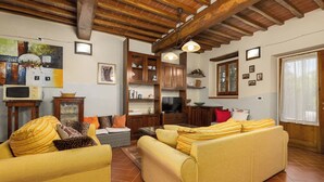 A living room with wooden beams, a sofa set, a television, and a fireplace. - Villa Morandi - Holiday Country Villa with swimming pool in Loro Ciuffenna, Tuscany (Loro Ciuffenna)
