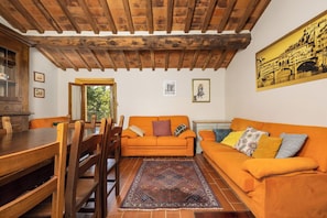 Una habitación con techo de madera, una mesa de comedor con sillas, un sofá naranja y un tapete estampado.