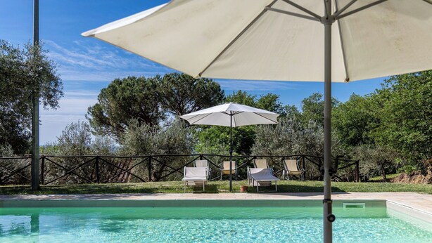 A swimming pool with lounge chairs and an umbrella, surrounded by trees and a fence. - Villa Morandi - Holiday Country Villa with swimming pool in Loro Ciuffenna, Tuscany (Loro Ciuffenna)