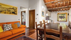 A cozy living room with a wooden dining table, orange sofa, and a large painting. - Villa Morandi - Holiday Country Villa with swimming pool in Loro Ciuffenna, Tuscany (Loro Ciuffenna)