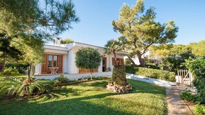 A house with a white exterior, wooden shutters, and a well-maintained garden with various trees and shrubs.