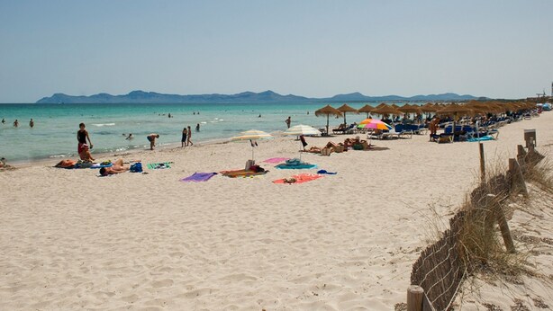 A beach with people sunbathing and swimming, umbrellas, and beach chairs.