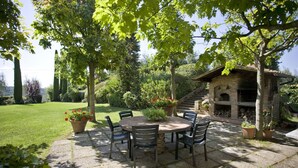 A patio with a round table and chairs, surrounded by potted plants and a stone fireplace.
