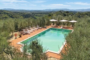 A rectangular swimming pool with a clear blue water surface, surrounded by a patio area with lounge chairs and umbrellas.